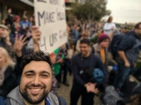 a man smiles while holding a sign in front of a crowd